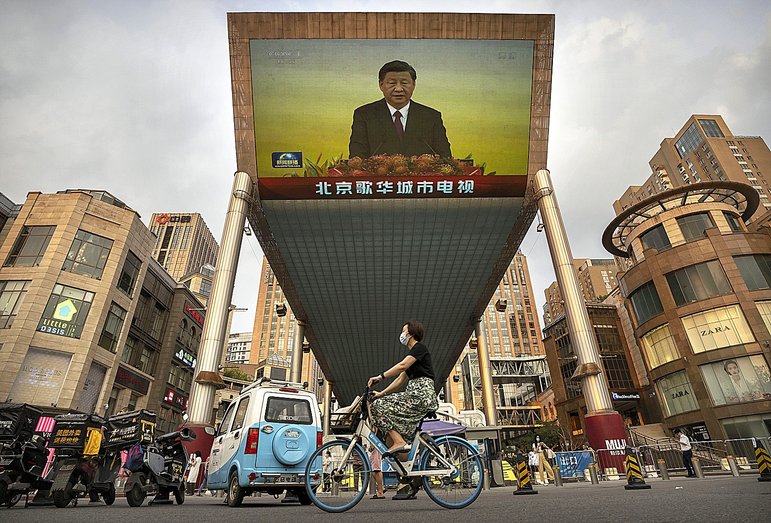 Una mujer en bicicleta pasa frente a una gran pantalla que proyecta un retrato de Xi Jinping.